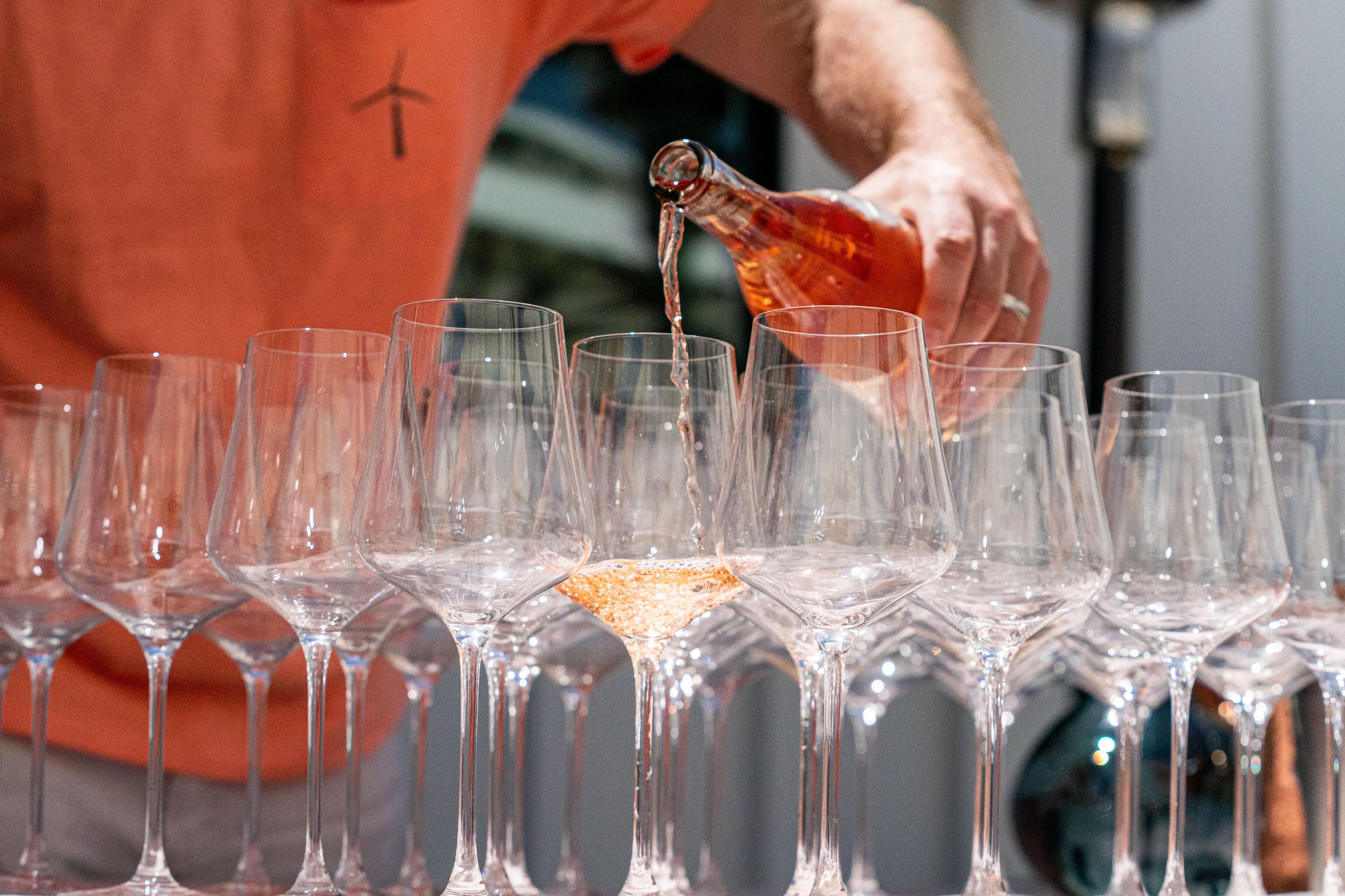Person wearing pink shirt pouring pink wine into glasses